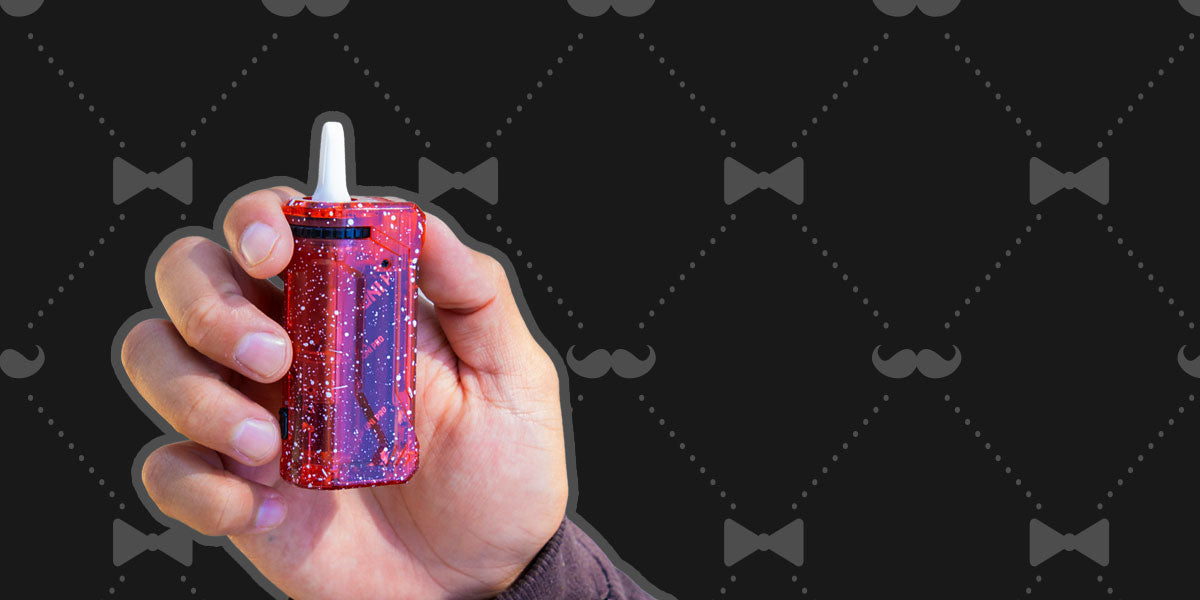 Hand holding a Wulf Mod X-Ray UNI Pro  device against a black background with mustache patterns.